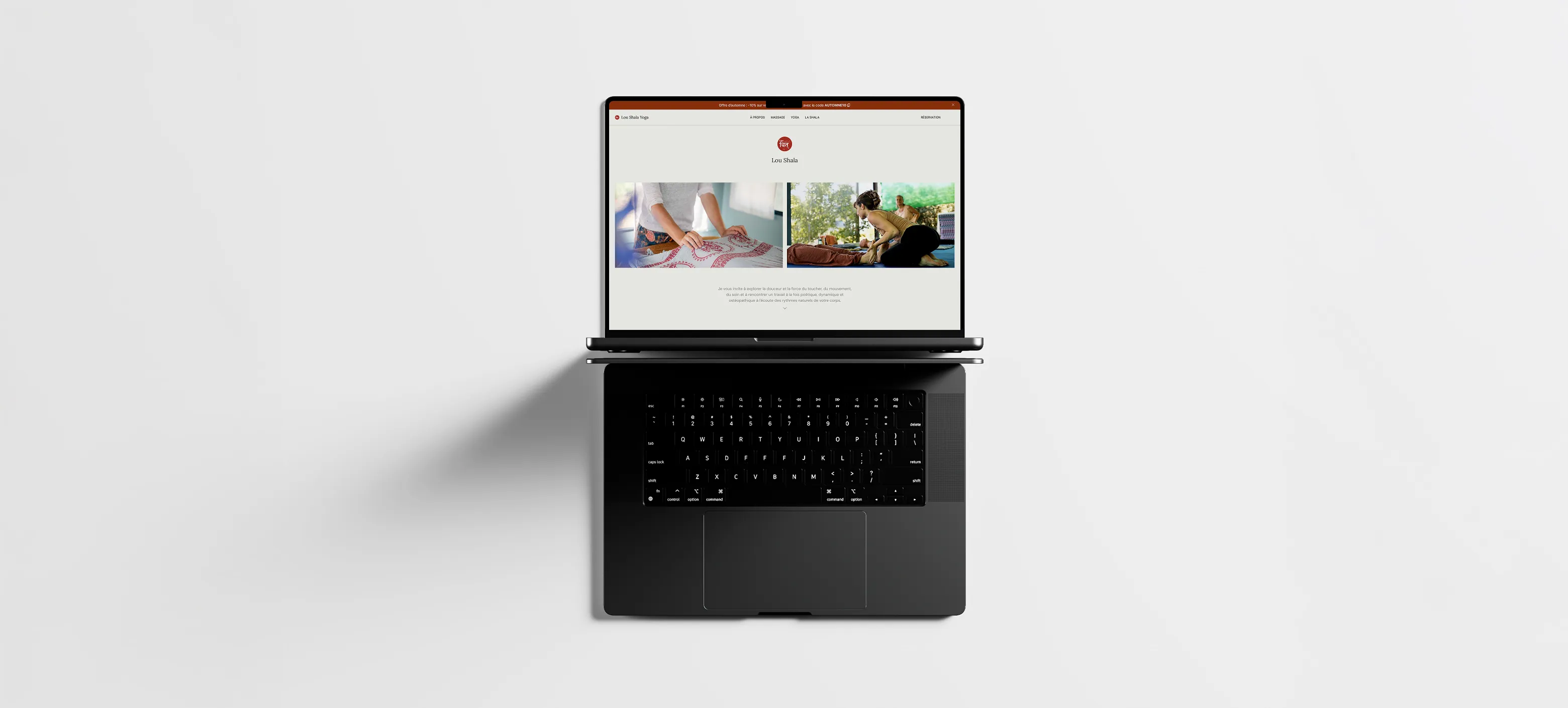 Top-down view of a black laptop on a white surface displaying a website with images of a person folding a patterned cloth and another person practicing yoga.